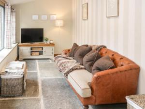 een woonkamer met een bruine bank en een televisie bij The Dovecote in Denbigh