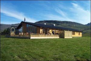 a large building in a field with a grass field at Eyjar Fishing Lodge in Breiðdalsvík
