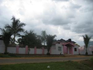 R&R Gardens Hotel في Mbale: بيت أبيض وأشجار النخيل خلف سور
