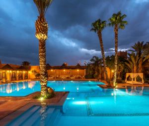a hotel pool with palm trees and lights at Berbère Palace in Ouarzazate