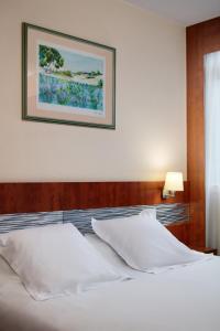 - un lit avec des oreillers blancs et une photo sur le mur dans l'établissement Hôtel & Résidence Octel, à Portet-sur-Garonne