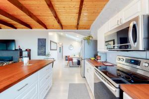 uma cozinha com armários brancos e um tecto de madeira em Strandhuisje em Rockaway Beach
