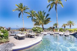 a swimming pool with chairs and palm trees at Hali'i Kai 3B in Waikoloa