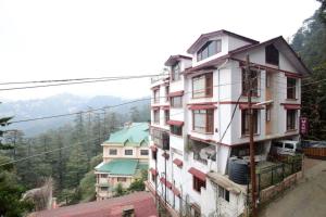 a tall white building with red windows on a hill at Goroomgo Marc Shimla Near Mall Road - Luxury Room - Excellent Service - Ample Parking - Best Hotel in Shimla in Shimla