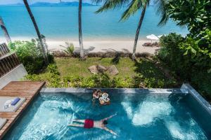 two people laying in a swimming pool next to a beach at NH Collection Samui Peace Resort in Bophut