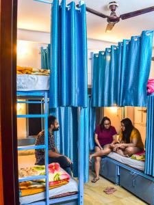 three people sitting on bunk beds in a room with blue curtains at Skyard Rishikesh, Laxman Jhula in Rishīkesh