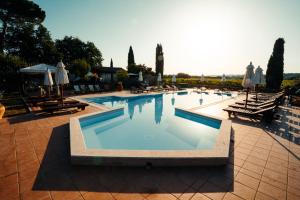 a large swimming pool with chairs and umbrellas at Villa Acquaviva Wine Resort in Montemerano