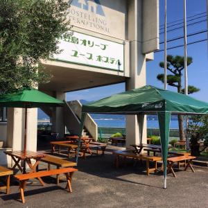 un grupo de mesas de picnic con sombrillas verdes fuera de un edificio en Shodoshima Olive Youth Hostel, en Shodoshima