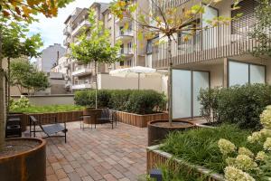 einen Innenhof mit Tischen, Stühlen, Bäumen und Gebäuden in der Unterkunft The Central City - Luxury ApartHotel in Luxemburg (Stadt)