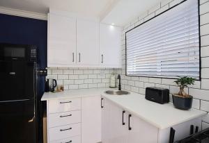 a white kitchen with a sink and a black refrigerator at Flatlet 2.1km from Iconic Blaauwberg Beach in Cape Town +16 photos