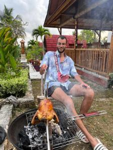 a man is cooking a chicken on a grill at Griyatama Bungalow in Nusa Penida