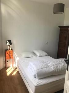 Una cama blanca en un dormitorio con una lámpara en una mesa en Villa refaite à neuf à 200 mètres de la plage en Soulac-sur-Mer