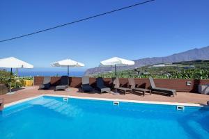 una piscina con sedie, ombrelloni e oceano di Finca Marina BuenVivir a Tazacorte