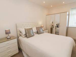 a white bedroom with a large white bed and a mirror at Top Of The Lane Luxury Holiday Apartment in Benllech
