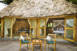 a resort with a thatched roof with two chairs and a bed at Gal Oya Lodge in Galgamuwa