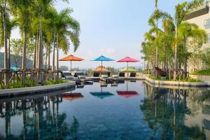 einen Pool mit Sonnenschirmen, Stühlen und Palmen in der Unterkunft Mida Grande Resort Phuket Official Account in Surin Beach