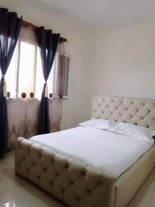 - une chambre avec un grand lit blanc et une fenêtre dans l'établissement Résidence Rosalie, à Yaoundé