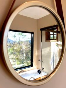 un miroir rond reflétant une salle de bains avec une fenêtre dans l'établissement Casa do Alto Santa Mônica- Natureza ao seu redor, à Itaipava