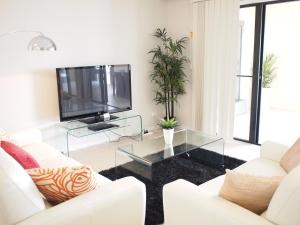a living room with white furniture and a flat screen tv at Edge Apartments Cairns in Cairns