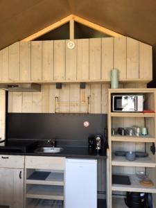 a kitchen with wooden cabinets and a sink and a microwave at Safari Lodge, glamping aan zee! in Callantsoog