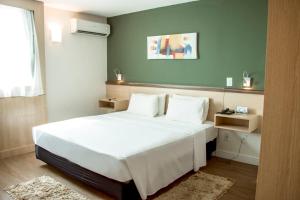Un dormitorio con una cama blanca y una pared verde. en Comfort Hotel Campos dos Goytacazes, en Campos dos Goytacazes