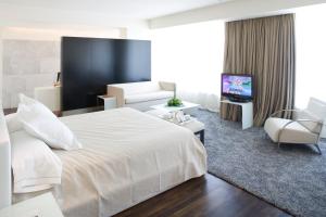 Habitación de hotel con cama blanca y sala de estar. en Parador de Alcalá de Henares en Alcalá de Henares