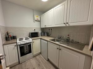 a kitchen with white cabinets and a sink and a stove at Cosy, 2 Bedroom Cottage in Guisborough Town Centre in Guisborough