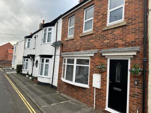 un bâtiment en briques avec une porte noire dans une rue dans l'établissement Cosy, 2 Bedroom Cottage in Guisborough Town Centre, à Guisborough