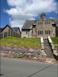 uma velha casa de pedra numa colina ao lado de uma rua em Cosy Arts & Crafts Cottage with stunning views em Brecon
