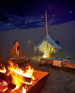 a man sitting over a fire with a tent in the background at Duna Camp Huacachina in Ica