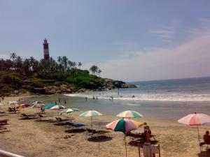 a beach with chairs and umbrellas and a lighthouse at Gokulam Homestay in Kovalam