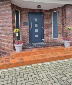 une maison en briques avec une porte noire et deux plantes en pot dans l'établissement Appartment Barbier, à Großefehn 