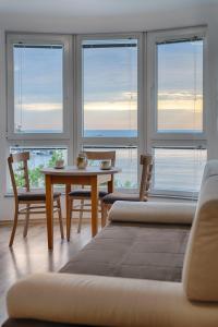 uma sala de estar com uma mesa, cadeiras e janelas em Moana Lighthouse Apartment em Ahtopol