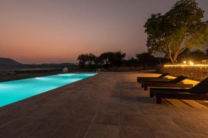 a row of benches next to a swimming pool at night at 1br Cottage with Pool - Lakeside Haven by Roamhome in Udaipur