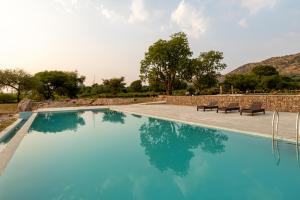 a blue swimming pool with two chairs and a wall at 1br Cottage with Pool - Lakeside Haven by Roamhome in Udaipur