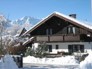 une maison recouverte de neige avec des montagnes en arrière-plan dans l'établissement Ferienwohnung Heimbeck Kochel, à Kochel am See