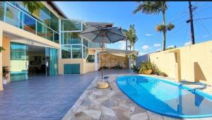 a swimming pool with an umbrella in front of a building at Praia com Conforto in Guaratuba