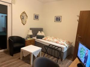 Habitación pequeña con cama, silla y TV. en Hotel Pension Wiesenau, en Bad Salzhausen