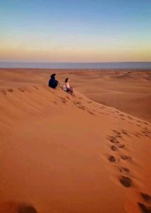 Ein Mann und eine Frau sitzen auf einer Wüste in der Unterkunft Auberge étoiles iriki in Foum Zguid