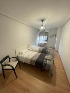 two beds in a room with a chair and a table at San Pablo, piso céntrico in Palencia