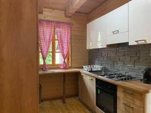 d'une cuisine avec des placards blancs, une cuisinière et une fenêtre. dans l'établissement Wooden house with a waterfall "Stipanov mlin", aux lacs de Plitvice