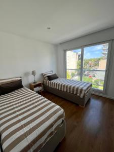 two beds in a room with a large window at Roca Trust II Semipiso de 3 ambientes para 4 personas en zona güemes con cochera in Mar del Plata