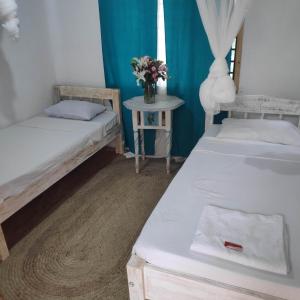 a room with two beds and a table with a vase of flowers at Sunny garden rooms Watamu in Watamu