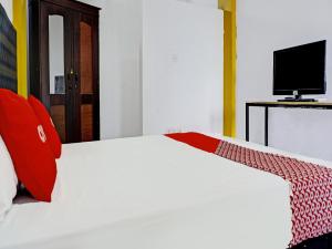 a bedroom with a white bed with red pillows and a television at OYO 91796 Guest House Ghalta Syariah in Karawang
