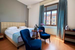 a bedroom with a bed and two blue chairs and a table at Hotel Zurigo Downtown in Lugano