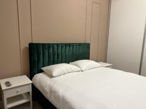 Mrs Smart Luxury Apartament في بلويستي: سرير مع اللوح الأمامي الأخضر بجوار طاولة