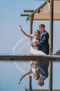 Una novia y un novio posando para una foto con su reflejo en Aegean Castle Andros – Adults Only, en Agia Eleousa