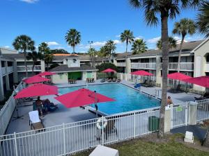 una piscina con sombrillas rojas y gente sentada a su alrededor en Newly Room in cozy hotel with Super location to the Parks en Kissimmee