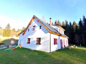 ein weißes Haus mit roten Fenstern auf einem grünen Feld in der Unterkunft Apartmány Na samotě in Kubohütten