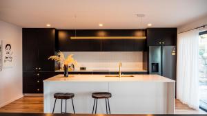 una cocina con armarios negros y una isla blanca con taburetes en Amazing view Architech Home 8Minutes to Hobart CBD, en Hobart